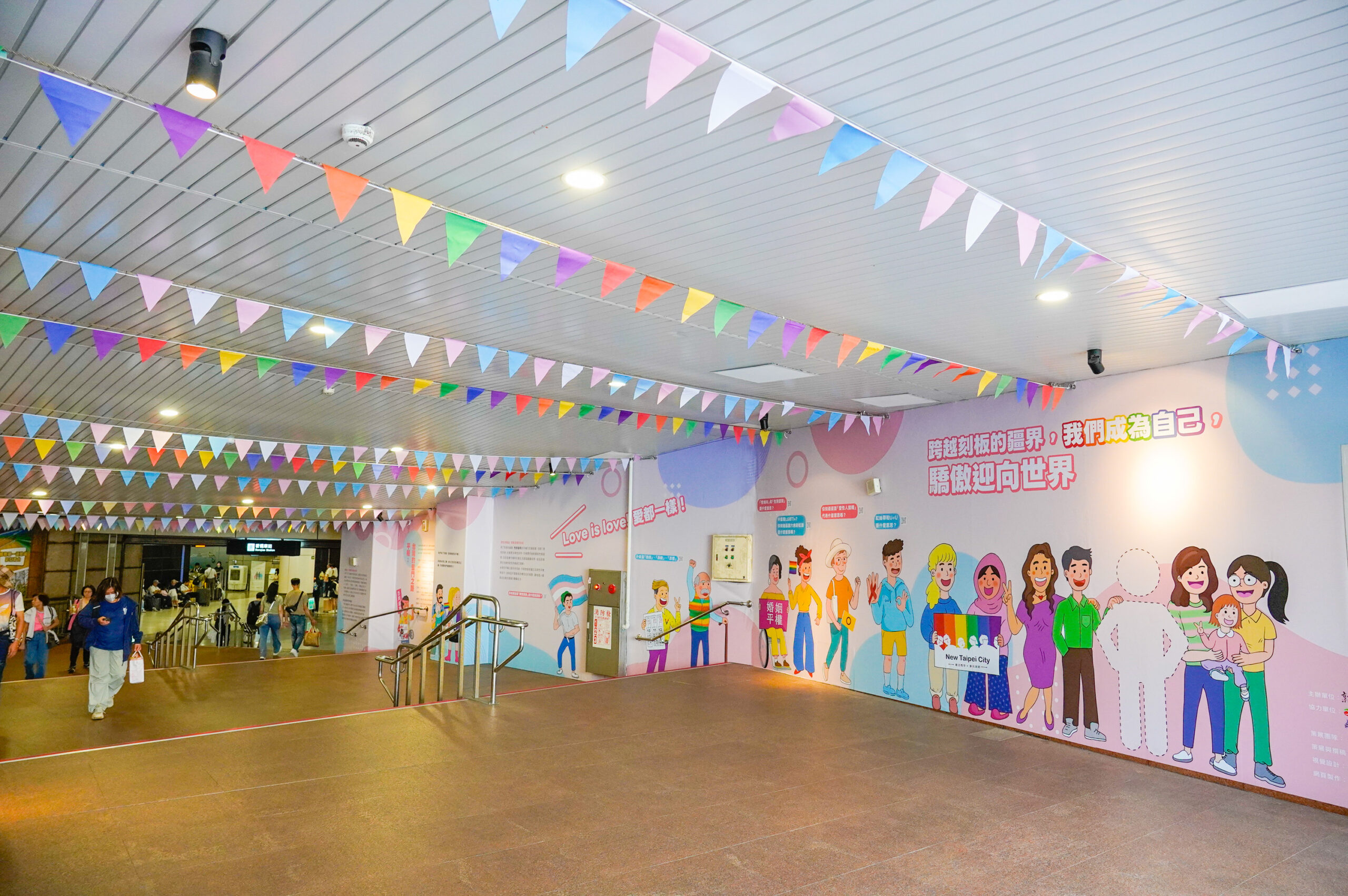 《圖說》今日至6月21日期間,「愛在新北・驕傲同行」特展於新北市民廣場往板橋車站的連通道展開,並懸掛多元性別友善旗幟,象徵城市裡的友善包容。〈社會局提供〉