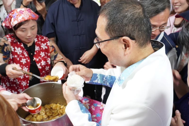 《圖說》侯友宜市長在活動現場的美食區與鄉親話家常,並品嚐客家菜包,氣氛熱鬧、溫馨。〈客家局提供〉